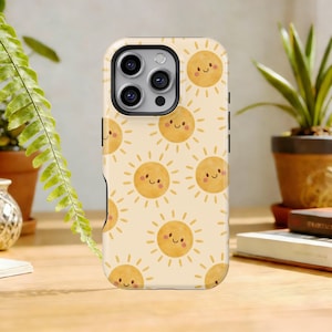 Op de afbeelding: Een telefoonhoesje met een herhaald patroon van lachende zonnen op een crèmekleurige achtergrond. De zonnen zijn geel met oranje stralen en kleine, lachende gezichten. De hoes heeft een zwarte rand rond de camera.