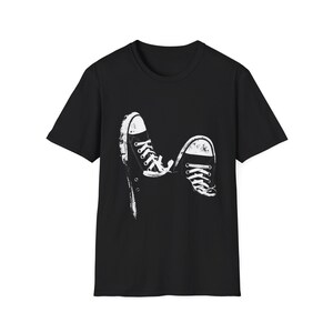 May include: Black t-shirt featuring a distressed white graphic of two sneakers, laces tied. The sneakers are depicted in a stylized, artistic manner. The design is centered on the shirt, creating a casual, everyday look.