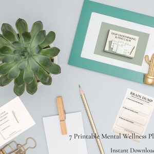 Può includere: Un set di 7 planner stampabili per il benessere mentale che include un foglio Brain Dump, una pianta succulenta verde, una cornice color ottanio con la scritta Stop Overthinking & Find Calm, una matita dorata, una molletta in legno e una clip dorata.