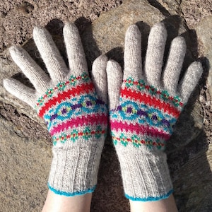 Puede incluir: Un par de guantes tejidos con un patrón geométrico colorido en tonos de azul, rojo, rosa y verde. Los guantes están hechos de una suave mezcla de lana beige.