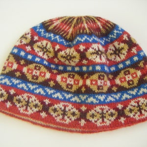 Op de afbeelding: Een gebreide muts met een geometrisch patroon in rood, bruin, blauw en wit.