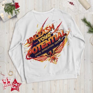Puede incluir: Sudadera blanca con el texto "UNLEASH YOUR POTENTIAL" en rojo, naranja y azul. El diseño incluye un gráfico de fénix y las palabras "DRIVE. DEDICATION. DESTINY."