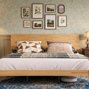 May include: A light-colored wooden bed frame with a rectangular headboard. The bed is dressed with a white sheet, a gray and white patterned throw blanket, and two decorative pillows featuring geometric and textured brown and white designs.