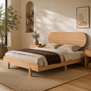 May include: A light-toned wooden bed frame featuring a rounded, oval-shaped headboard and low-profile legs. The bed is dressed with neutral-colored linens, including a light beige duvet cover and a dark brown textured throw blanket draped across.