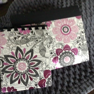 May include: Two rectangular spiral-bound notebooks featuring a repeating floral pattern in shades of magenta, light pink, gray, and white. The notebooks have black plastic spiral bindings at the top and a black header strip on the larger notebook.