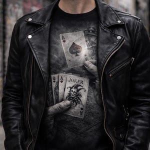 May include: Black leather jacket with a zipper closure and a black t-shirt featuring a playing card design. The t-shirt graphic includes the Ace of Spades and a Joker card. The image has a dark, moody aesthetic.