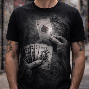 May include: Black t-shirt featuring a playing card design. The design includes an Ace of Spades, a pocket watch, and a hand holding playing cards, including a Joker card. The shirt has a crew neck and short sleeves.