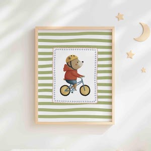May include: A framed print depicting a cartoon bear on a blue bicycle, wearing a yellow helmet and red hoodie. The print is set against a green and white striped background, with wooden stars and a crescent moon on the wall.