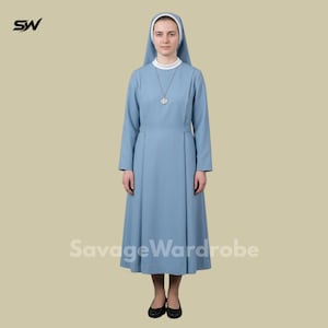 Puede incluir: Un hábito de monja azul claro con cuello blanco y velo a juego. El vestido de manga larga presenta un diseño modesto y un colgante plateado. El logotipo de SavageWardrobe es visible en la parte inferior de la imagen.