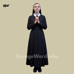 May include: A full-length black habit with a white collar and wimple. The nun's outfit includes a long-sleeved dress and a head covering. The person is standing with hands clasped in prayer. The SavageWardrobe logo is visible.