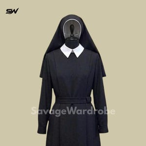 May include: A black nun habit with a white collar and a matching belt. The habit includes a long-sleeved dress and a head covering. The text "SavageWardrobe" is visible on the garment.