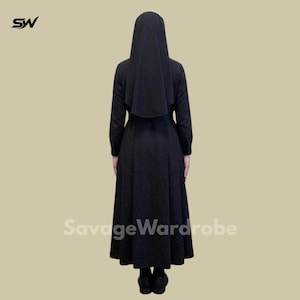 May include: A black nun's habit, including a long-sleeved dress and a matching head covering. The back view of the outfit is shown, with the text "SavageWardrobe" visible. The outfit is made of a dark fabric.