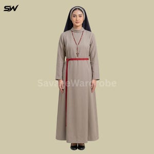 May include: A long-sleeved, floor-length beige dress with a high neckline, paired with a dark blue head covering. A thin red belt cinches the waist, and a brown beaded rosary with a cross pendant hangs around the neck. The outfit includes black shoes.
