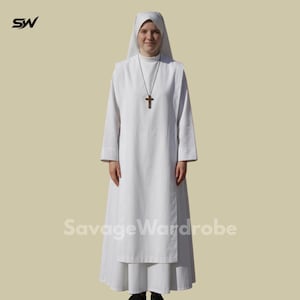 Puede incluir: Un hábito religioso blanco, que incluye una túnica de manga larga, un tocado y un colgante de cruz. El texto "Savage Wardrobe" es visible en la prenda. El atuendo lo lleva una persona.