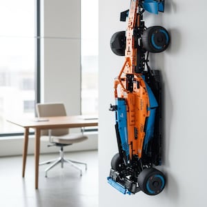 May include: A model race car in orange and blue is mounted on a white wall. The model has large black tyres, a detailed chassis, and aerodynamic features. The car is a replica of a Formula 1 vehicle.