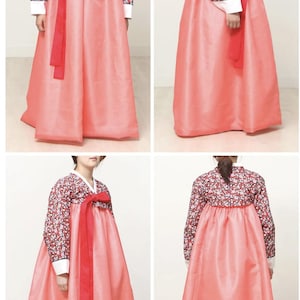 May include: A traditional Korean hanbok dress. The dress features a long, flowing coral skirt and a floral patterned top with long sleeves. A long red sash is tied at the waist. White trim accents the sleeves and neckline.