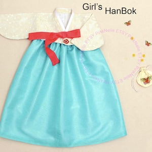 May include: A traditional Korean Hanbok dress for girls. The dress features a light blue skirt, a cream-colored top with a red bow, and the text "Girl's Hanbok". Decorative butterflies and a small pouch are also visible.
