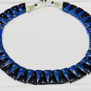 May include: A striking necklace featuring alternating triangular blue and black stones. The stones are arranged in a collar style, connected by a silver-toned clasp. The necklace is a bold statement piece.