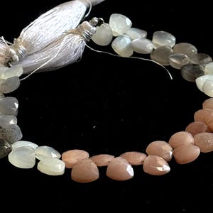 May include: A strand of heart-shaped beads in shades of gray, peach, and white. The beads are strung together, with a white tassel at the top. The beads are approximately 0.5 inches in size.