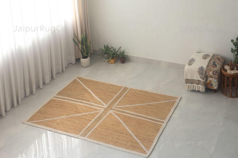 May include: A rectangular jute rug with a geometric design. The rug features a natural tan color with white lines forming a pattern reminiscent of a flag. The rug is placed on a light-colored floor, suitable for home decor.
