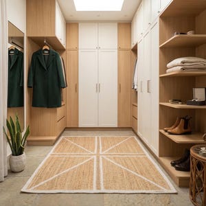 May include: A walk-in closet with light wood and white cabinetry, open shelving, and a jute rug with a geometric design. A dark green coat hangs in the closet. The room has a neutral color palette.