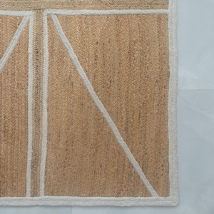 May include: A rectangular jute rug with a Union Jack design. The rug features a natural tan background with a white and tan geometric pattern. The border is white, and the rug is placed on a light gray surface.