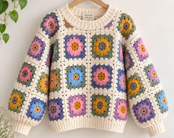 Puede incluir: Un suéter de manga larga confeccionado con hilo color crema que presenta un patrón repetitivo de cuadrados granny. Cada cuadrado contiene un motivo floral multicolor en tonos rosa, amarillo, azul y morado, enmarcado por bordes crema.