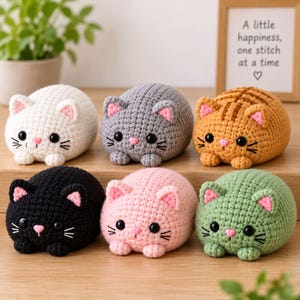 May include: Six small, round, crocheted cat plushies in white, gray, orange tabby, black, pink, and light green. Each cat features black plastic eyes, a small pink nose, embroidered whiskers, and pink-lined ears. The plushies are arranged in two rows.