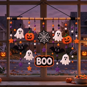 Op de afbeelding: Een Halloween-wandhanger met gehaakte figuren van witte spoken, oranje pompoenen, zwarte vleermuizen, paarse en oranje sterren en een spinnenweb, opgehangen aan een houten stok. Een centraal zwart bord met oranje rand toont het woord BOO.