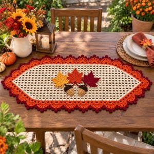 May include: An oval crochet table runner featuring a cream-colored mesh center decorated with three crocheted autumn leaves in yellow, orange, and dark red, paired with two small brown acorns. The border consists of scalloped orange and dark red yarn.