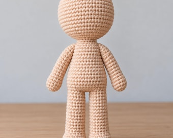 Op de afbeelding: Een beige gehaakte poppenbasis met een groot rond hoofd, een cilindervormig lichaam, twee armen en twee benen. De gehele figuur is gemaakt met een consistent, strak steekpatroon in huidkleurig garen, wat zorgt voor een gladde, uniforme textuur.
