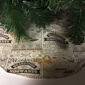 May include: A cream-colored round tree skirt with a brown and white print of the words "Quidditch at Hogwarts" and illustrations of Quidditch equipment. The skirt has a distressed, vintage look.