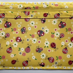 May include: A yellow fabric zippered pouch with a ladybug print. The pouch has a white and black trim around the edges.