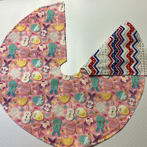 May include: A pink and white fabric tree skirt with a pastel Easter egg and bunny pattern. The skirt has a matching fabric insert with a red, white, and blue chevron pattern.