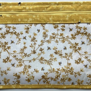 May include: A yellow zippered pouch with a white fabric lining featuring a pattern of brown branches and bees. The pouch has a yellow zipper and a yellow border.
