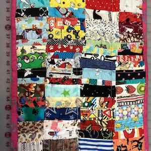 May include: A patchwork quilt with a pink border. The quilt is made of rectangular fabric pieces with various patterns, including cartoon characters, paw prints, and musical notes. The quilt measures approximately 30 inches by 40 inches.