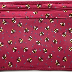 May include: A pink zippered pouch with a clear plastic window. The pouch has a repeating pattern of bees and small blue dots.