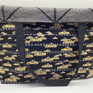 May include: Black tote bag with yellow taxi cab print. The bag has black straps and a white polka dot pattern on the top flap.