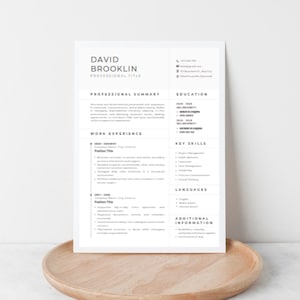 May include: A resume titled "David Brooklin" with sections for professional summary, work experience, education, key skills, languages, and additional information. The resume is on a white paper, resting on a light brown wooden tray.