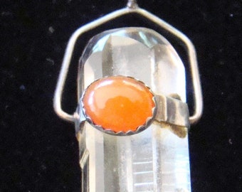 May include: A silver chain necklace with a clear quartz crystal pendant. The pendant is set in a silver frame with a small orange carnelian stone in the center.