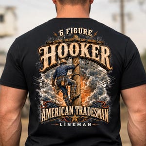 Puede incluir: Una camiseta negra con un gráfico en la espalda de un liniero subiendo a un poste eléctrico. El texto dice 6 FIGURE HOOKER, AMERICAN TRADESMAN y LINEMAN. El diseño incluye nubes de tormenta, rayos y cables eléctricos en una ilustración.