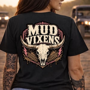 Może przedstawiać: Czarny t-shirt z grafiką na plecach przedstawiającą napis MUD VIXENS białymi literami nad beżową czaszką byka. Wzór zawiera różowe błyskawice, brązowe plamy błota i czarne ślady opon umieszczone wewnątrz ozdobnej ramki.