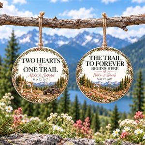 May include: Two round white ornaments hanging from a branch, featuring a mountain landscape, floral borders, and text. The left ornament reads "TWO HEARTS ONE TRAIL MIKE & SARAH MAY 22, 2027" with an off-road vehicle. The right reads "THE TRAIL TO FOREVER BEGINS HERE MIKE & SARAH MAY 22, 2027."