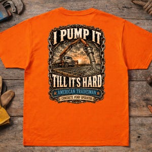 May include: A bright orange t-shirt featuring a graphic on the back. The design shows a concrete pump truck at a construction site, enclosed in a chain-link border. Text reads: I PUMP IT TILL IT'S HARD, AMERICAN TRADESMAN, CONCRETE PUMP OPERATOR.