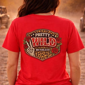 May include: A red t-shirt with a graphic design on the back. The design features the words "PRETTY WILD" in a vintage font, surrounded by roses and a leopard print background. The text "MV FUEL & CO" is also included.