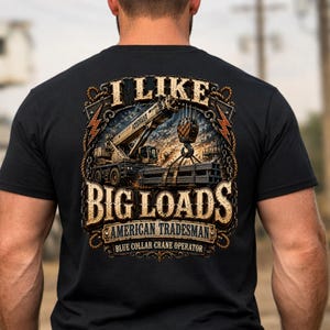 May include: A black t-shirt featuring a graphic on the back of a construction crane lifting steel beams. The text reads I LIKE BIG LOADS, AMERICAN TRADESMAN, and BLUE COLLAR CRANE OPERATOR. The design is framed by a rope border with lightning bolts.