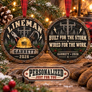 May include: Two round ornaments with a rusted metal border and red ribbon hangers. The left ornament features a yellow hard hat, pliers, a utility pole, and the text LINEMAN GARRETT 2026. The right ornament displays a utility pole, lightning bolts, and the text BUILT FOR THE STORM, WIRED FOR THE WORK, GARRETT 2026.