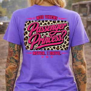 May include: A purple t-shirt featuring a graphic on the back with a leopard print rectangle. The text reads MUD VIXENS, Passenger Princess?, and NEVER. I DRIVE. in bright pink script and block lettering, accented by small pink stars.