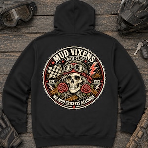 May include: A black hooded sweatshirt featuring a circular graphic on the back. The design includes a skull wearing goggles and a bandana, flanked by red roses, a checkered flag, and lightning bolts, with the text MUD VIXENS TRAIL CLUB EST 2026.