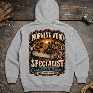 Op de afbeelding: Een lichtgrijze hoodie met een afbeelding op de achterkant. Het ontwerp toont een kettingzaag, boomstammen en een bos in een kettingrand. De tekst luidt: MORNING WOOD SPECIALIST, AMERICAN TRADESMAN en BLUE COLLAR LOGGER.